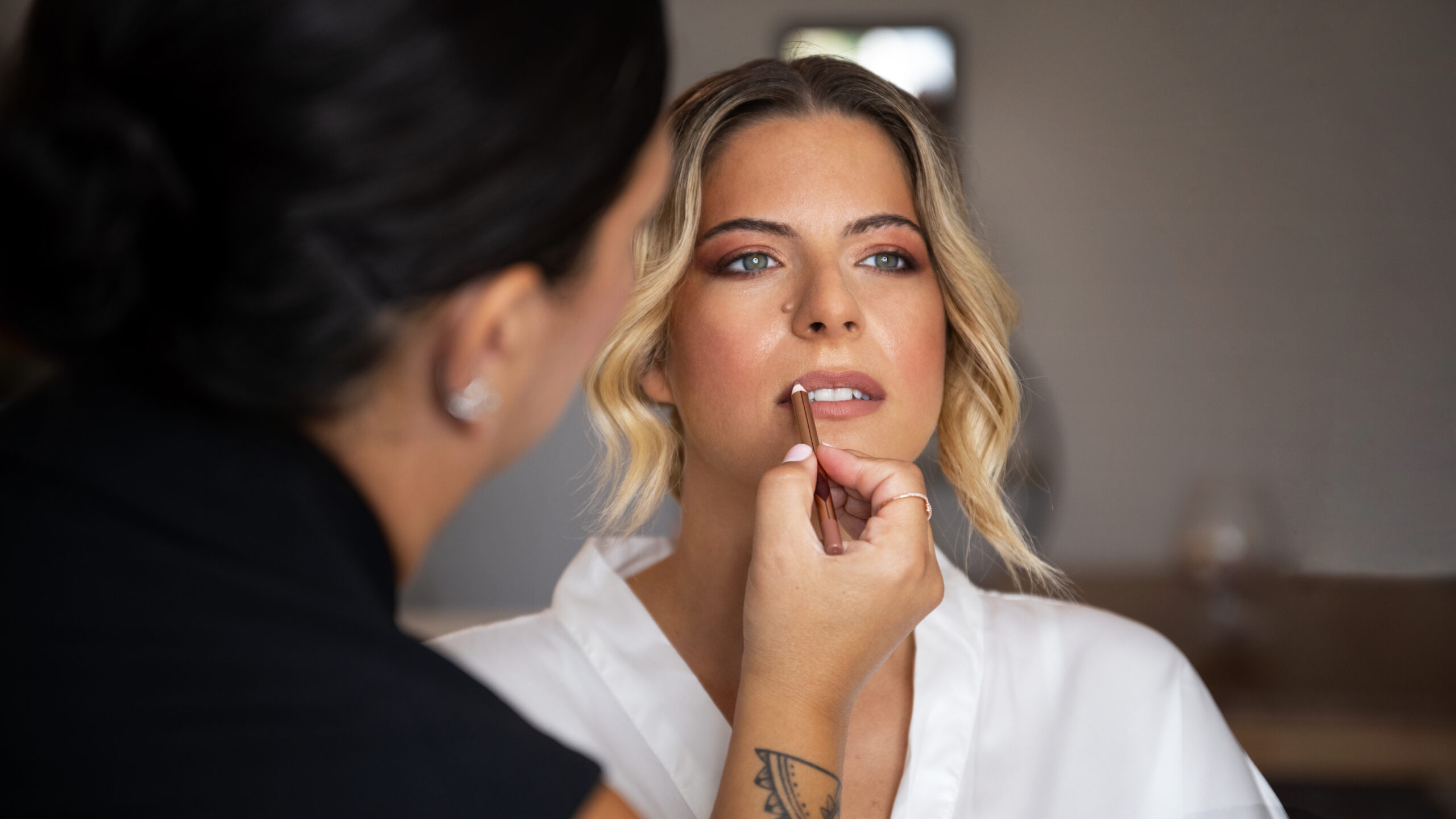 A professional makeup artist is doing lip-pigmentation of the young female patient.