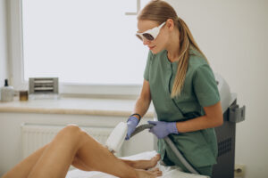 Woman performing laser hair removal on a client's leg.